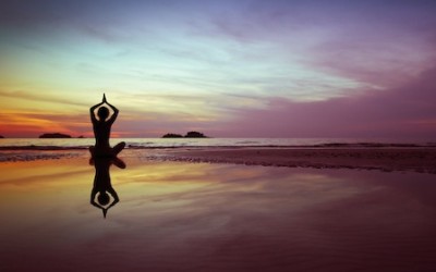 woman practices yoga on the beach at sunset