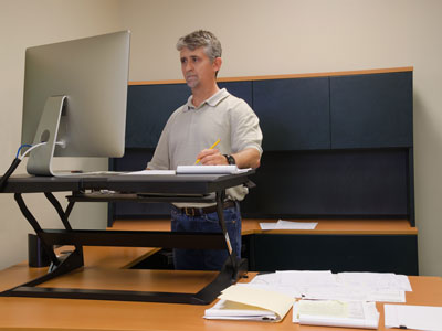 A man works at an ergonomic standing desk with proper posture.